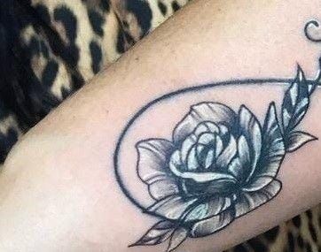 a black and white rose tattoo on the left arm, with an arrow in the middle