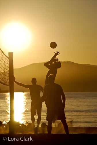 three people playing volleyball on the beach at sunset or sunrise, while the sun is setting