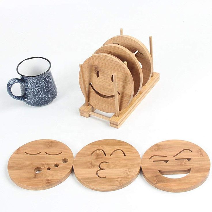 four wooden coasters with faces drawn on them next to a cup and saucer