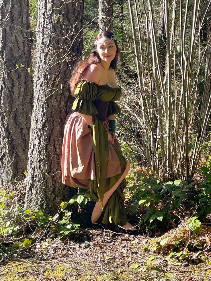 a woman dressed in an old fashioned dress standing next to a tree and some branches