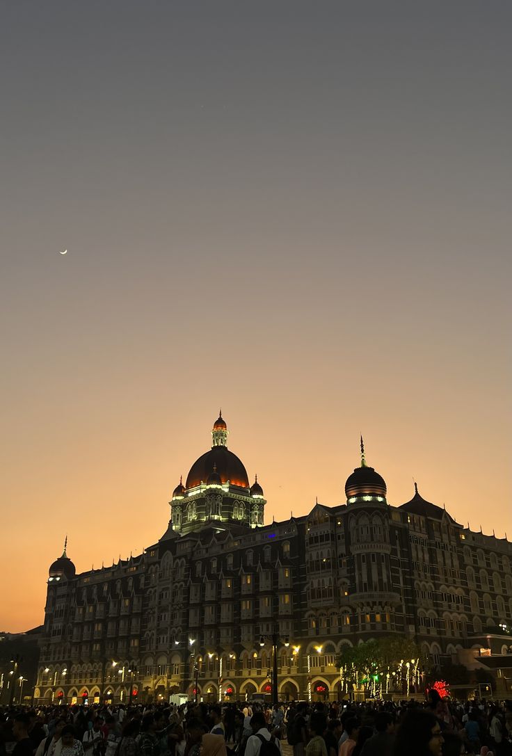 people are standing in front of a large building at night with the moon behind it