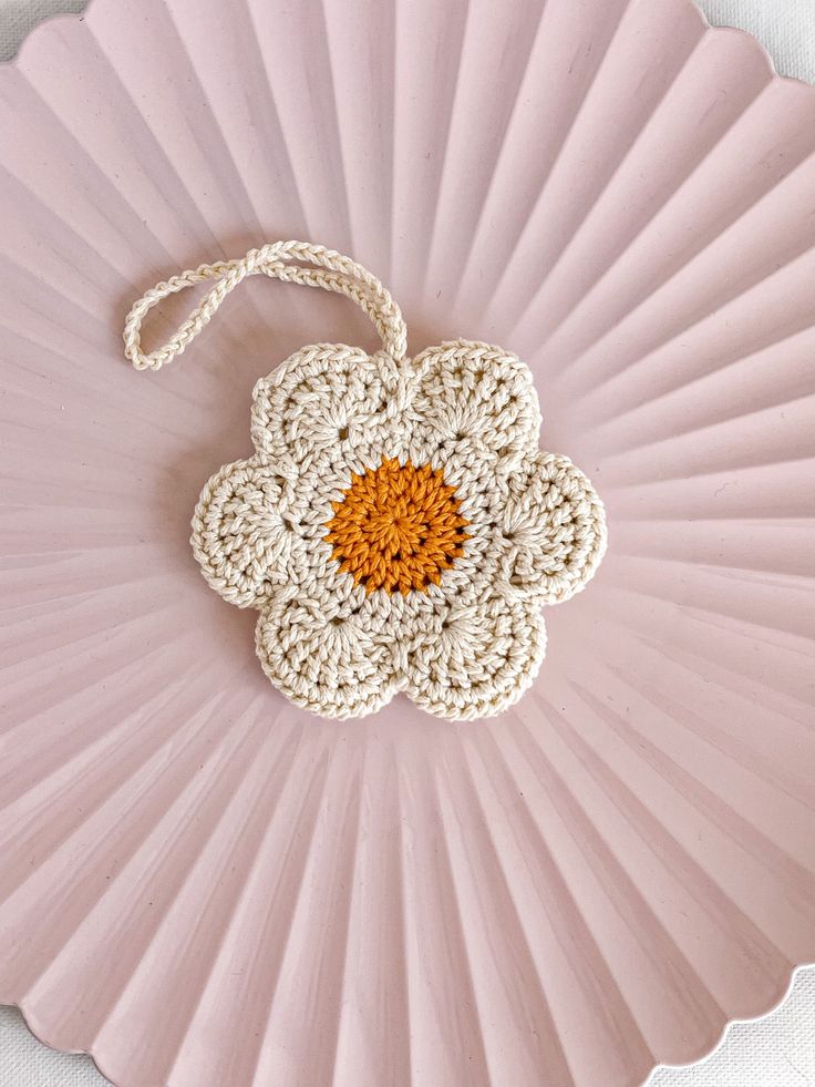 a crocheted doily with an orange center sits on a pink plate against a white background