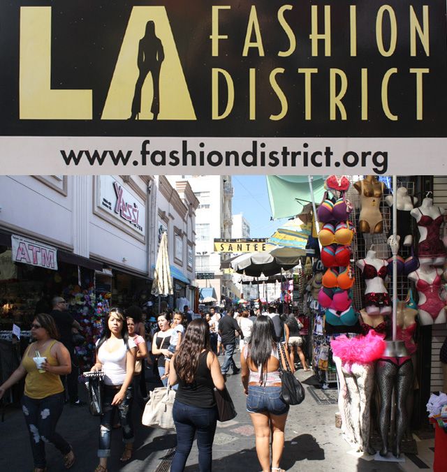 people are walking down the street in front of fashion district storefronts and signs