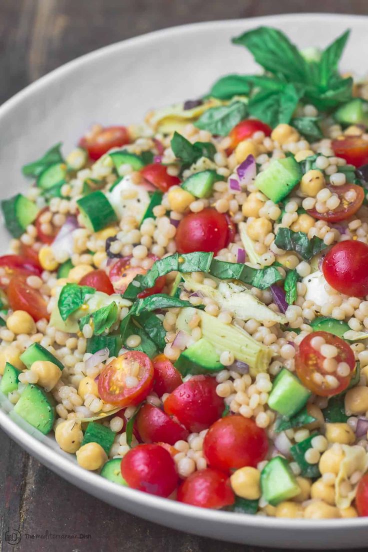 a white bowl filled with couscouse, tomatoes and cucumbers on top of a wooden table