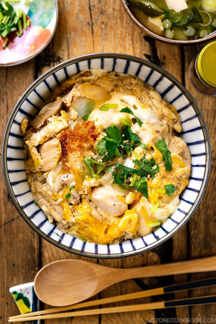 a bowl filled with food on top of a wooden table next to cups and spoons