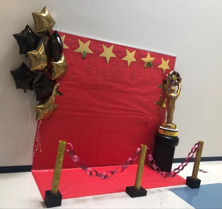 a red carpet with black and gold stars on it next to a trophy, balloons and streamers