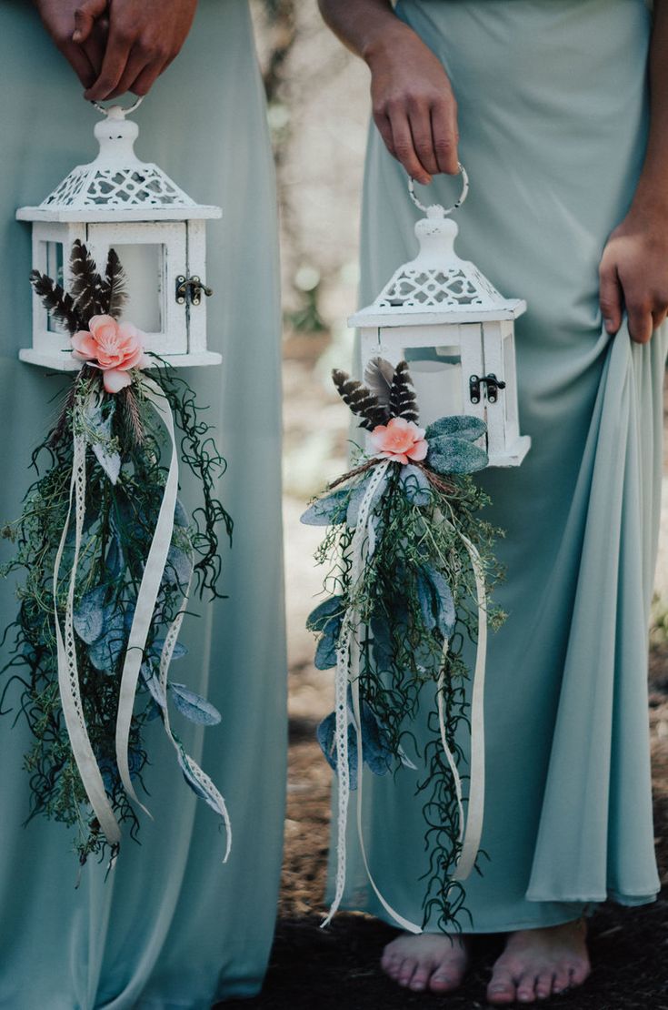 two bridesmaids in blue dresses holding birdcages with flowers and greenery