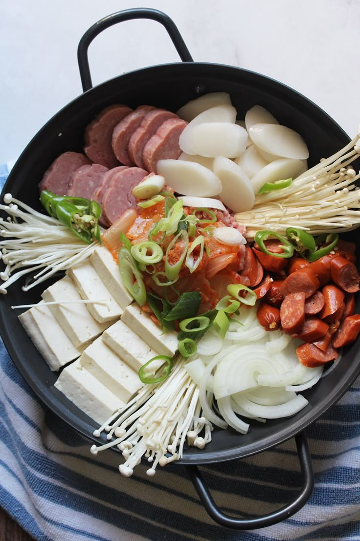 a pan filled with meat and vegetables on top of a blue striped towel next to a wooden table