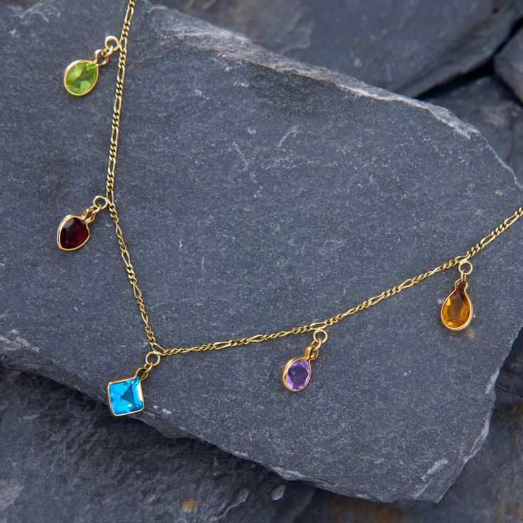 This bejeweled station necklace features a pinch bezel-set oval cut peridot, heart cut garnet, square cut blue topaz, round cut amethyst, and pear cut citrine that dangle from an 18 inch long baby figaro chain. The necklace is crafted in 14k yellow gold and finished with a spring ring clasp. Gold Multi-stone Fine Jewelry Gemstones, Gold Multi-stone Gemstones In Fine Jewelry Style, Gold Multi-stone Jewelry For May Birthstone, Luxury Drop Multi-stone Jewelry, Dainty 14k Gold Multi-stone Jewelry, Gold Gemstones With Accents For May Birthstone, 14k Gold Birthstone Necklace With Gemstone Accents, Gold Gemstones For May Birthstone, 14k Gold Jewelry With Gemstone Accents And Dangle Shape