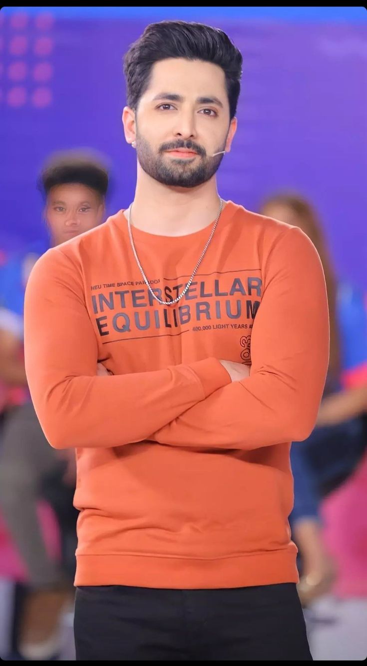 a man in an orange shirt is standing with his arms crossed