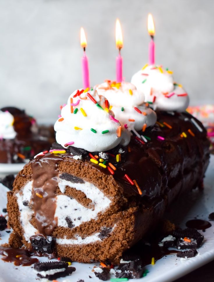 a chocolate roll with white frosting and sprinkles on it is sitting on a plate