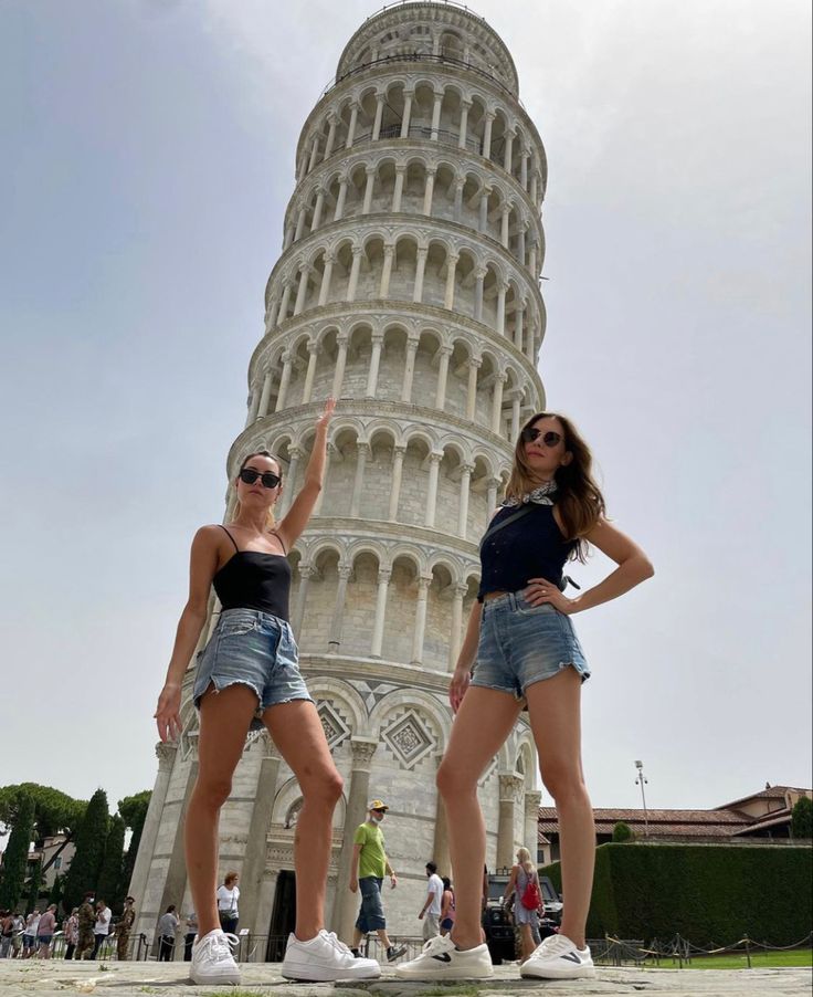 two beautiful young women standing in front of a tall tower with a clock on it's side