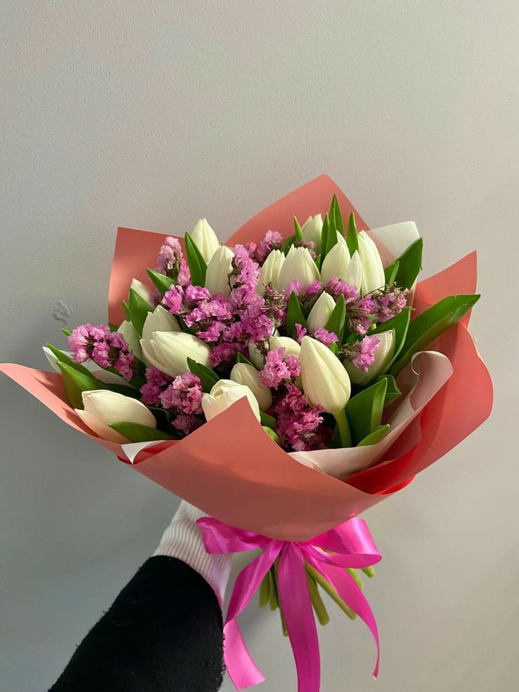 a hand holding a bouquet of white and pink tulips