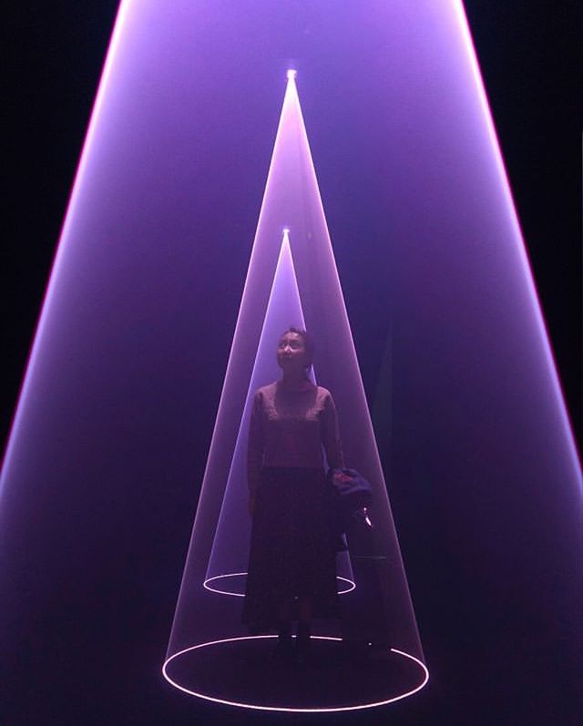 a woman standing in front of a purple light with her hands on her hips and looking up