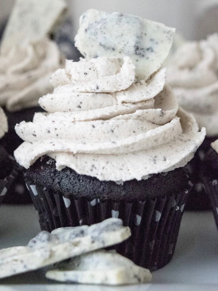 cupcakes with white frosting and oreo cookies on the side are shown