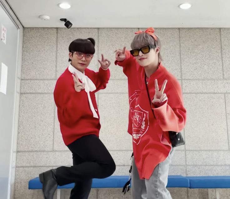 two young men in red sweaters and black pants posing for the camera with their hands up