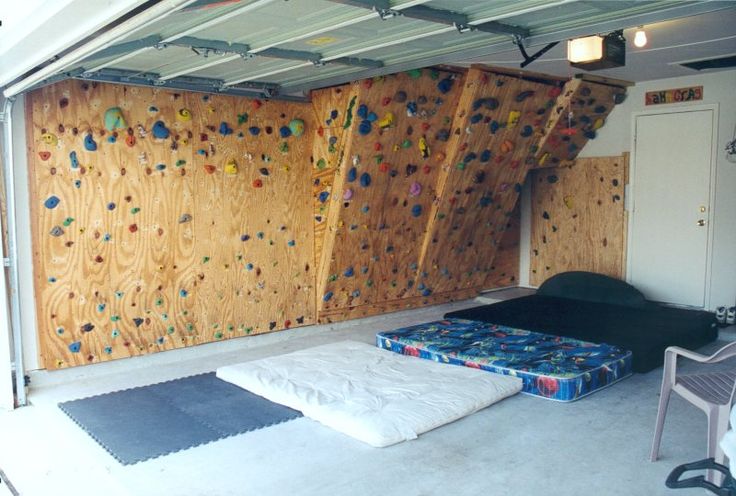 an indoor climbing wall in a garage with two mattresses on the floor next to it