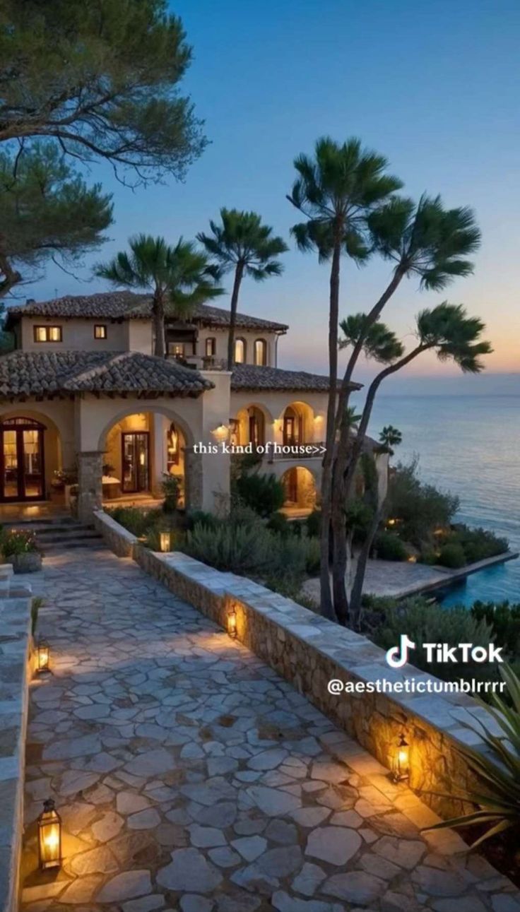 a large house with lots of lights in front of the water and trees at dusk