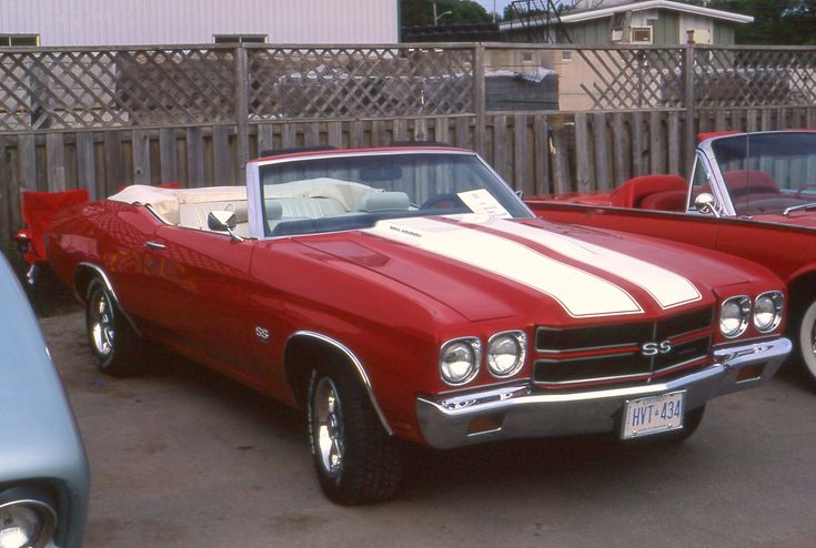 two red and white cars parked next to each other in a parking lot with wooden fence