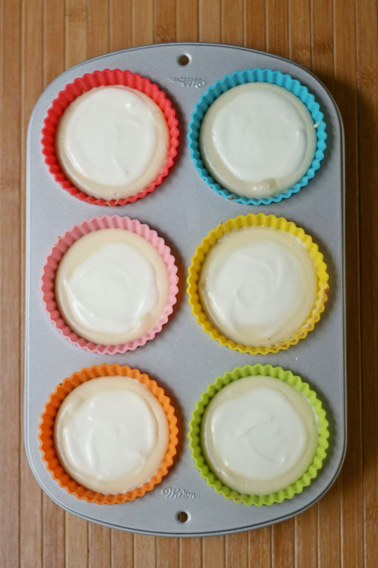 six cupcakes with white frosting sitting in a muffin tin on a wooden table