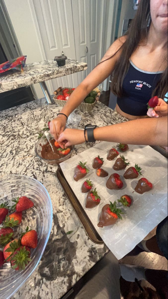 a woman cutting up strawberries on top of a white counter next to a plate of chocolate covered strawberries