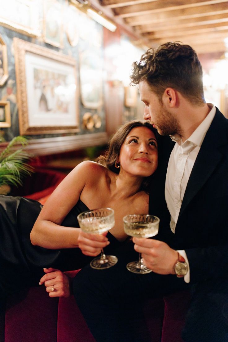 a man and woman sitting next to each other holding wine glasses