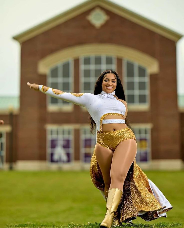 a woman in a gold skirt and white top is dancing on the grass with her arms out