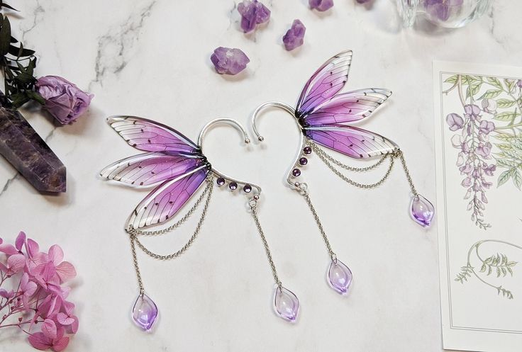 two purple fairy wings hanging from chains next to some flowers and cards on a table