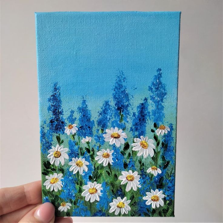 a painting of daisies and bluebells is being held up by a hand