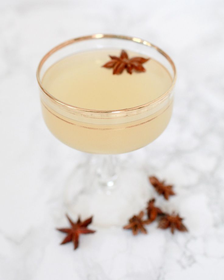 a drink in a glass with an orange garnish on the rim next to some cinnamon stars