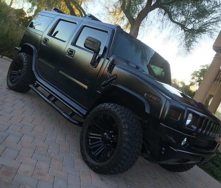 a black hummer truck parked on the side of a brick road in front of some trees