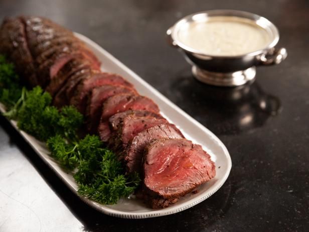 some meat is on a white plate and garnished with parsley next to a silver bowl