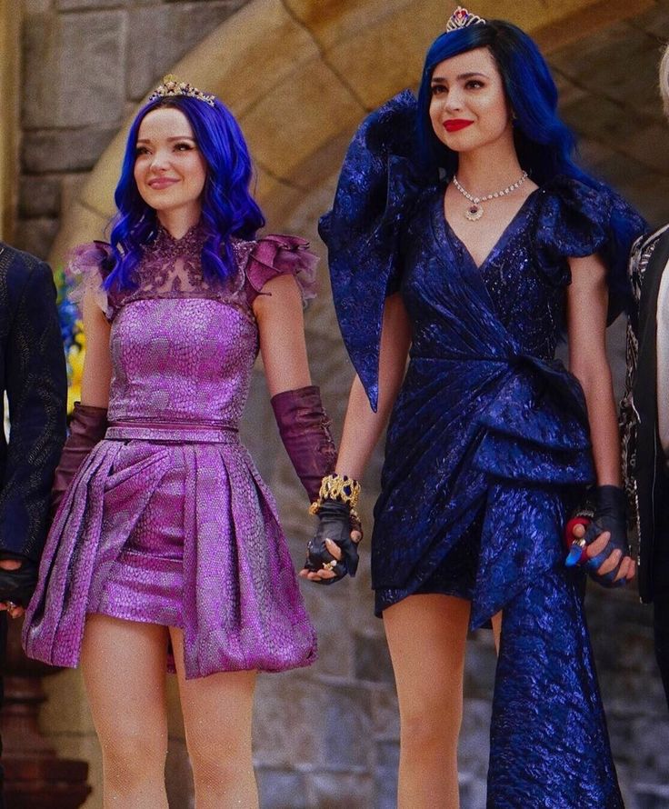 two women in purple dresses holding hands and walking down the street with other people behind them