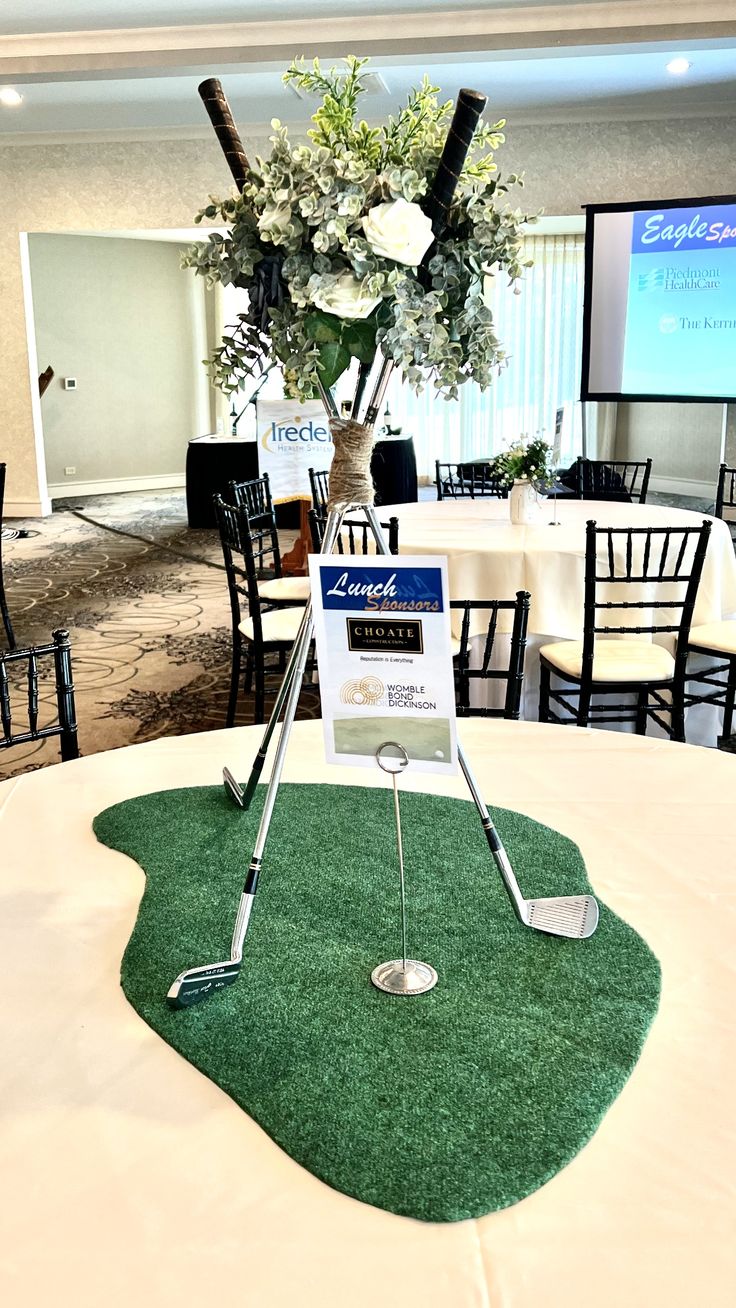 a golf themed centerpiece on top of a round table in a banquet room with white tables and black chairs