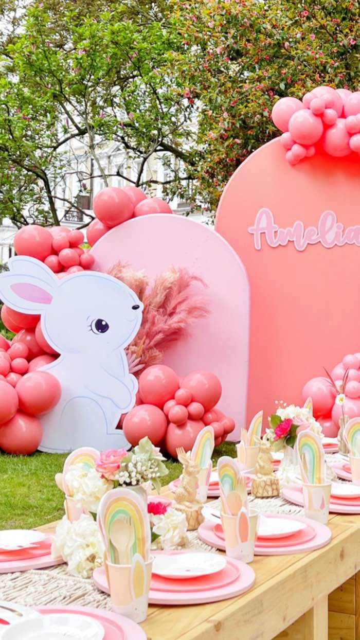 a table set up with pink balloons, plates and napkins in the shape of rabbits