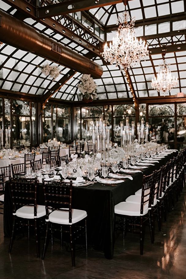 a large dining room set up with black and white table cloths, chandeliers and chairs