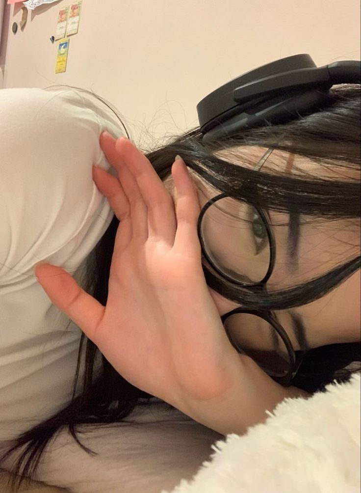 a woman laying on top of a bed with her hands over her head and glasses