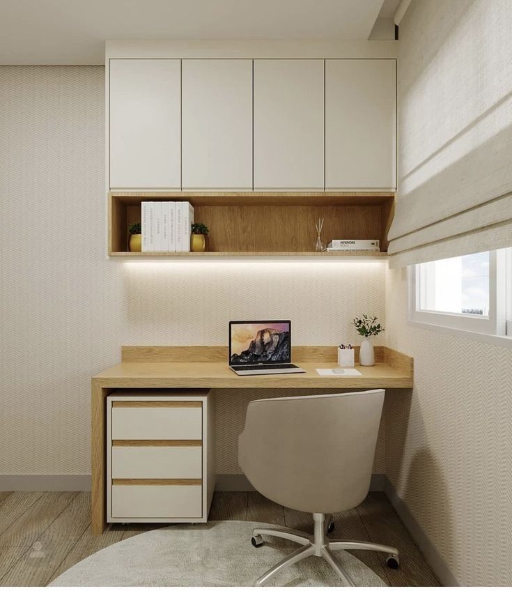 a desk with a laptop on top of it next to a white cabinet and window