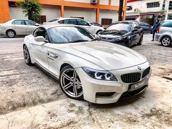 a white bmw z4 is parked in front of some other cars on the street