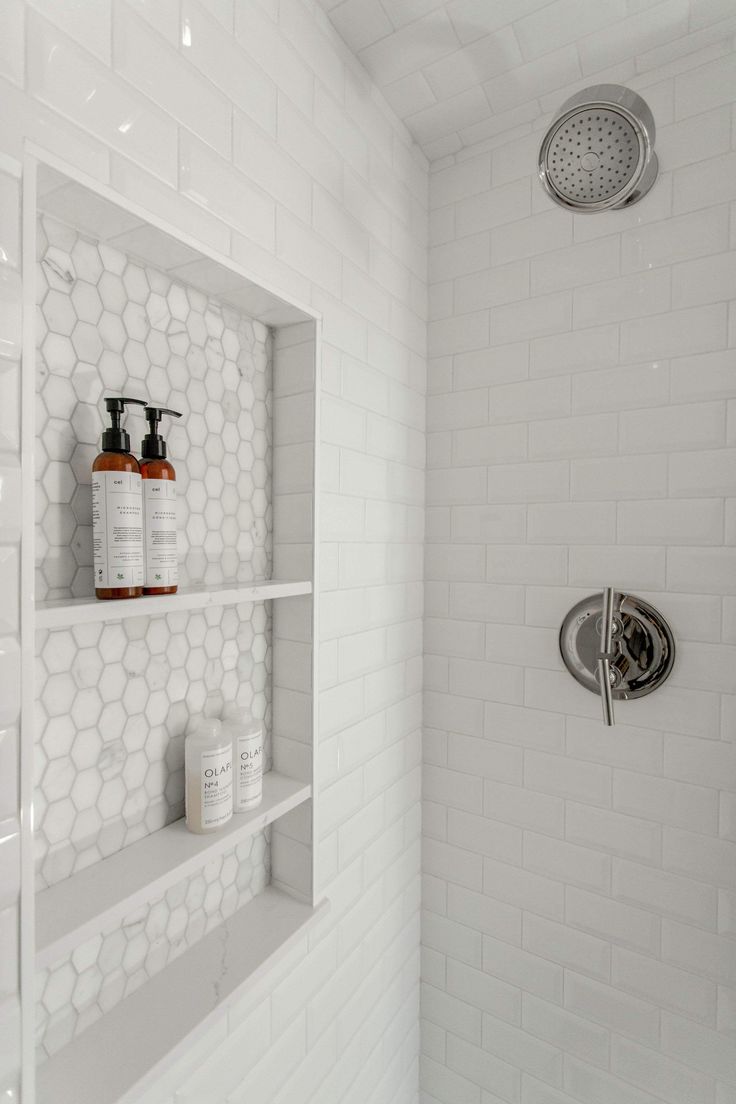 a white tiled shower with shelves holding soap and shampoos on the wall next to it