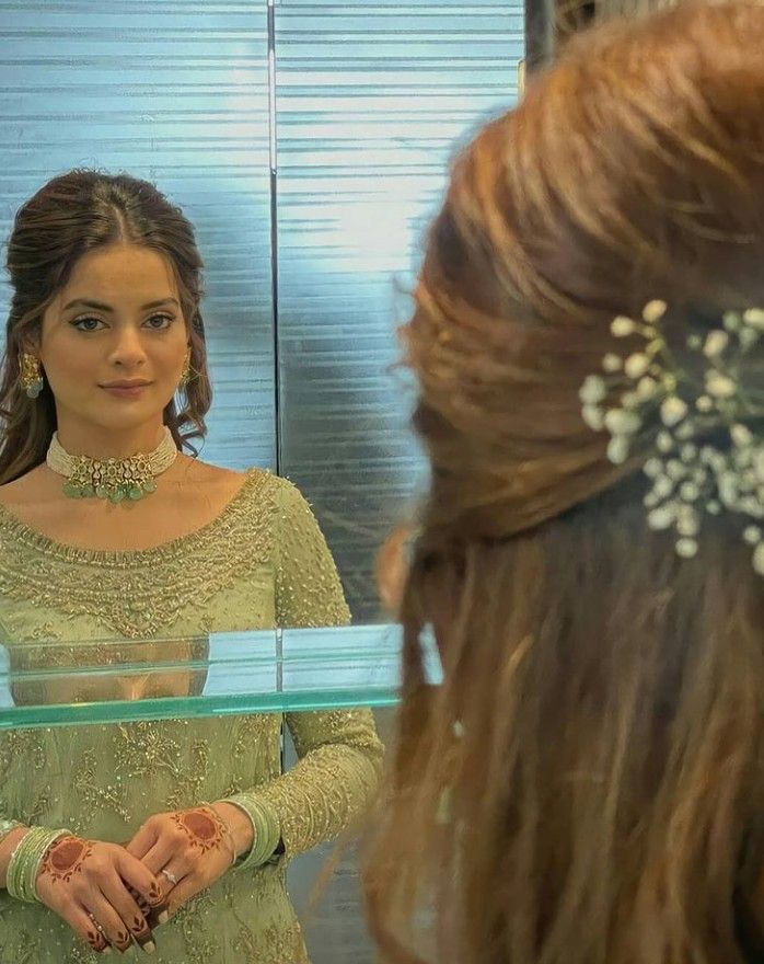 a woman standing in front of a mirror wearing a green dress and holding her hands together