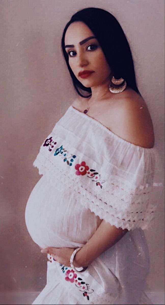 a pregnant woman in a white dress posing for the camera with her hands on her hips