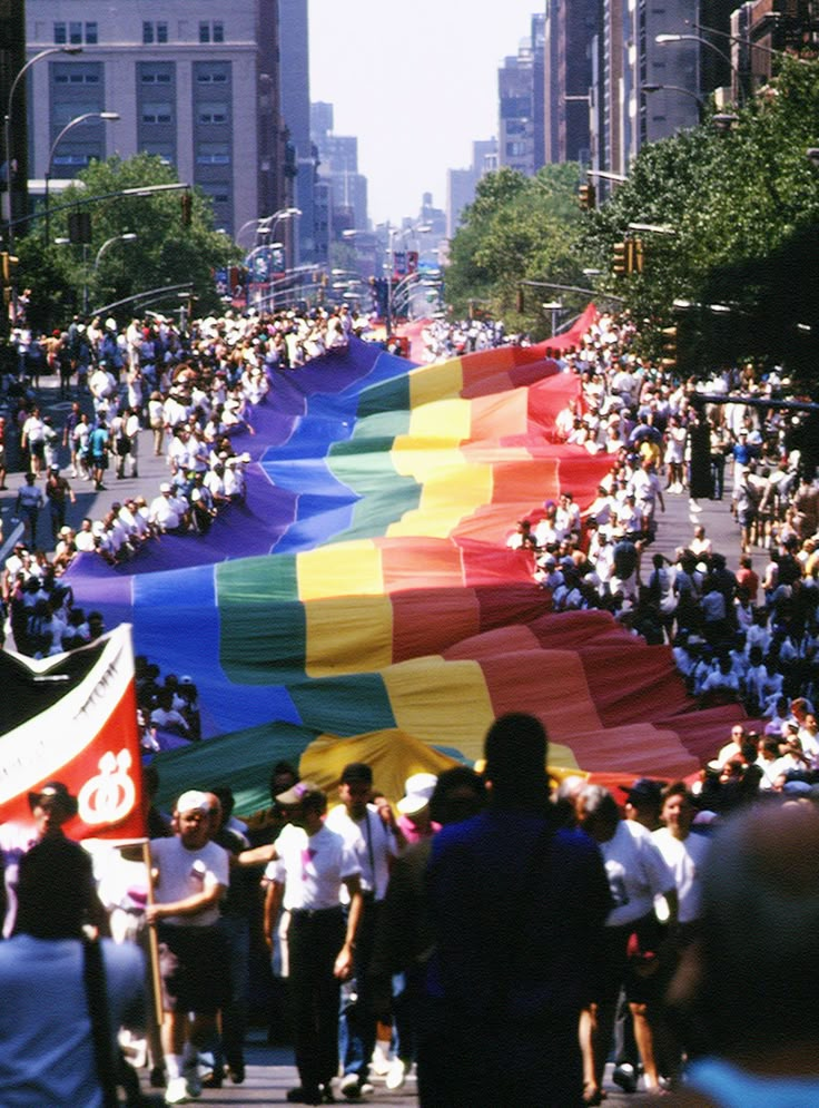 a large rainbow flag is being carried down the street