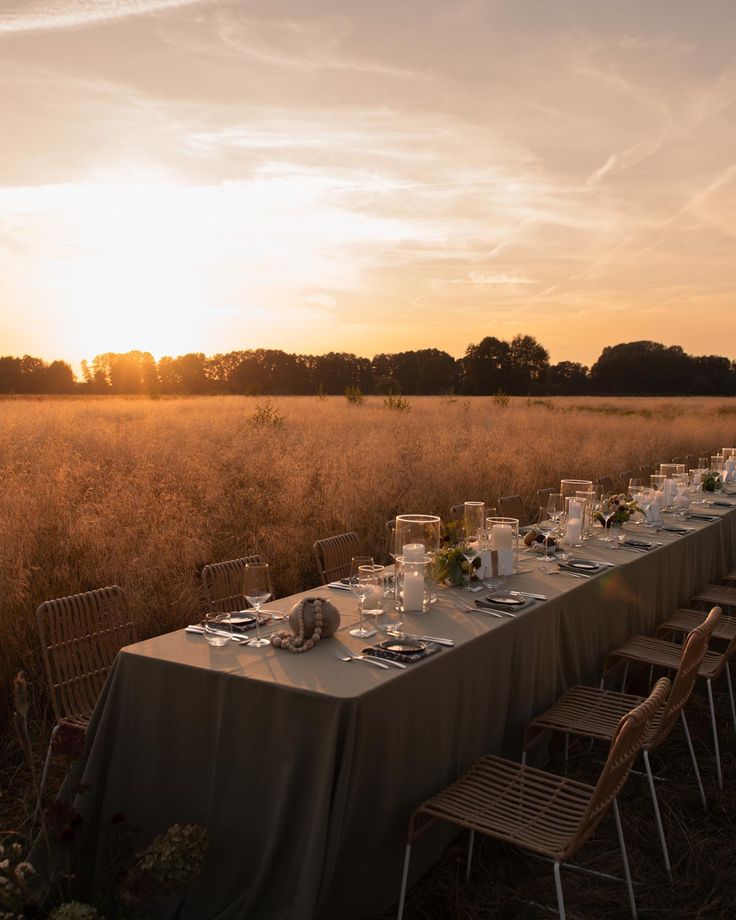 a long table is set up in the middle of a field at sunset with candles on it