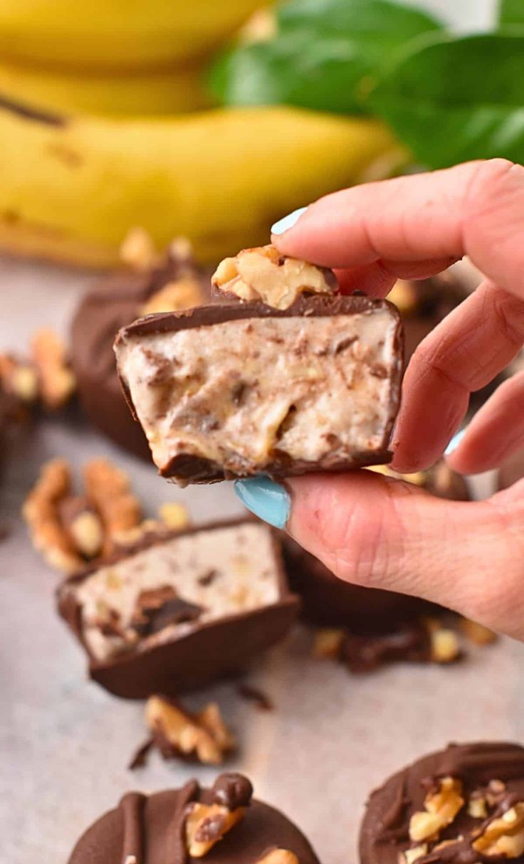 a hand holding a piece of chocolate peanut butter fudge with walnuts on the side