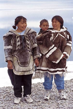 two women standing next to each other on top of a rocky hill with snow in the background