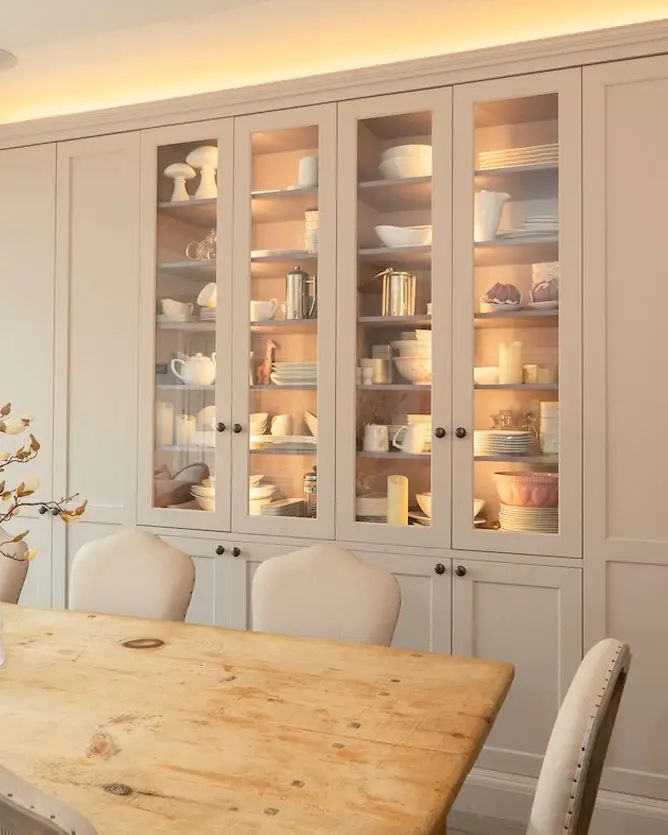 a wooden table sitting in front of a white cupboard filled with plates and bowls on top of it