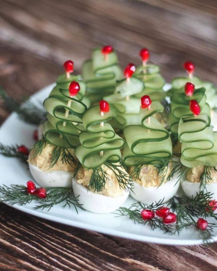 deviled eggs topped with cucumbers and christmas greenery on a white plate