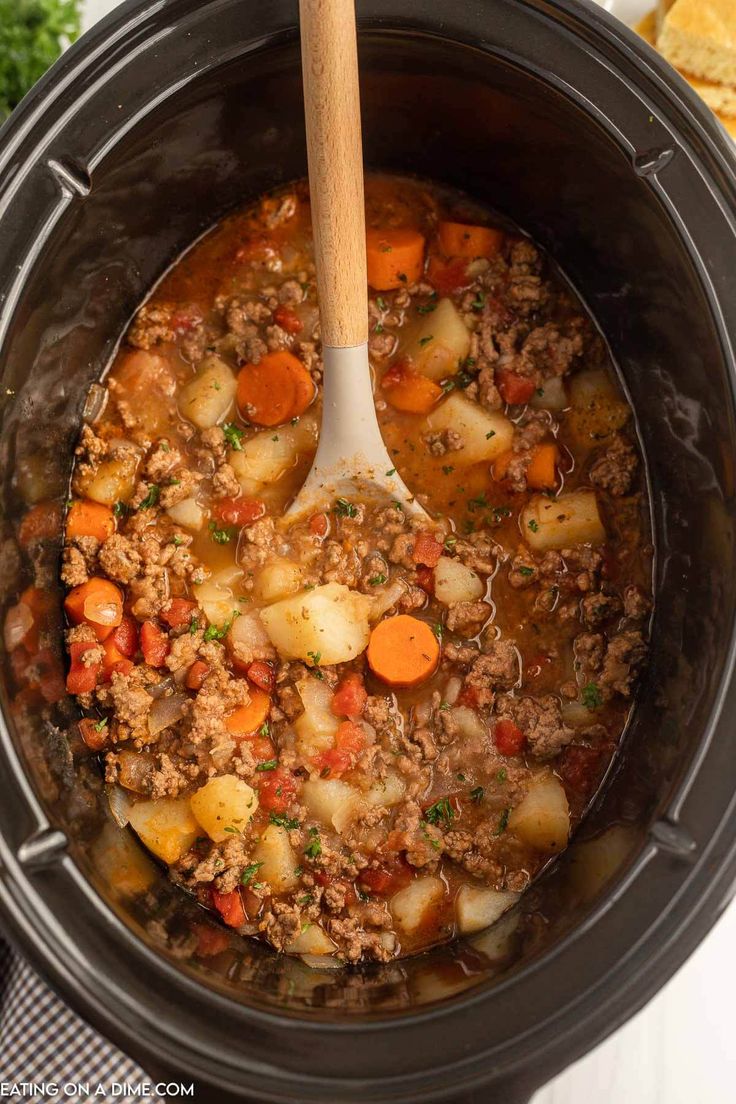 a crock pot filled with ground beef and carrots next to some crackers