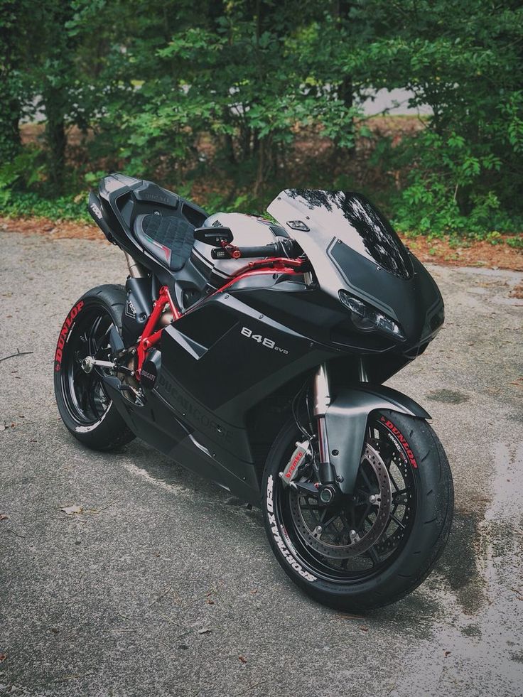 a black motorcycle parked on top of a parking lot in front of some green trees